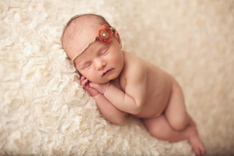 A newborn baby girl on a white floral fabric backdrop with a pearl and floral tieback.