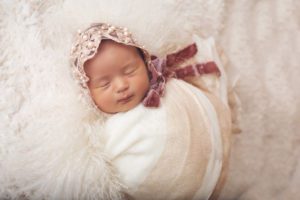 Ailani looks heavenly wrapped in cream with a pale pink pearl velvet bonnet on a bed of cream lambswool