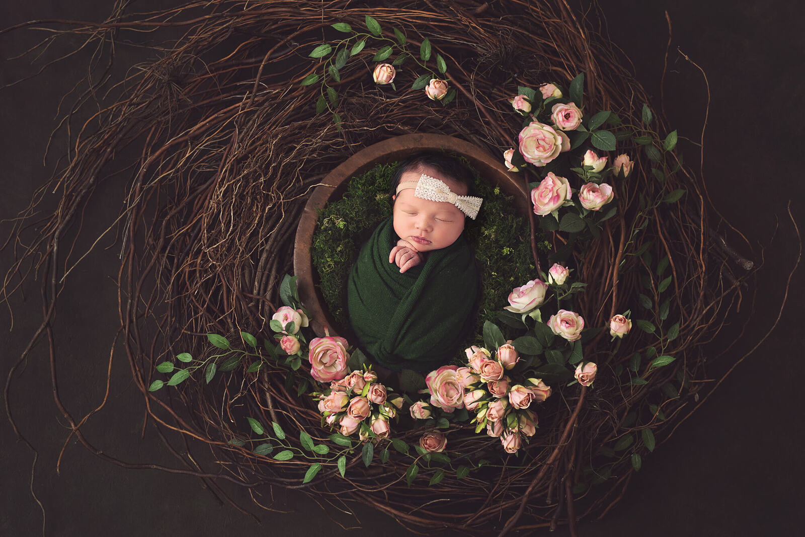 Newborn surrounded by pink roses in a bed of moss