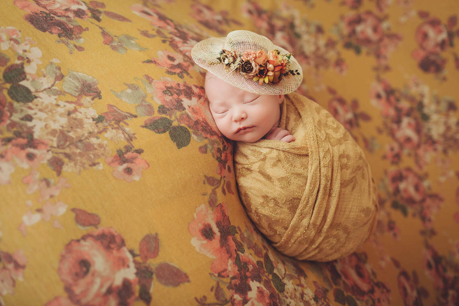 Baby Stella wearing a tiny hat wrapped in a golden yellow wrap on a golden yellow floral backdrop during her newborn session with Belle Vie Photography in Wiesbaden