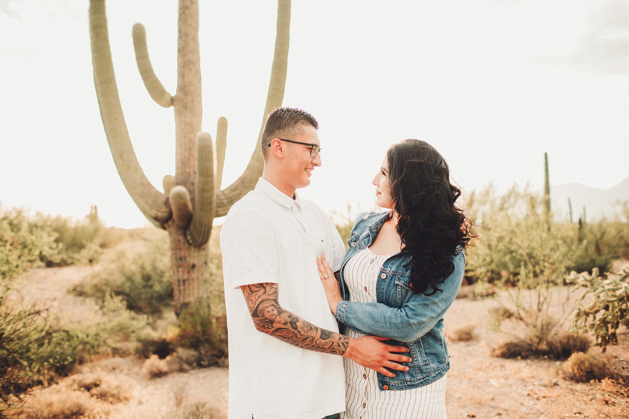 A husband and wife during their sunset family session with a giant saguaro and the setting sun.