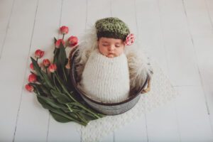 Baby Amelia in a bucket with fresh tulips and a green beret