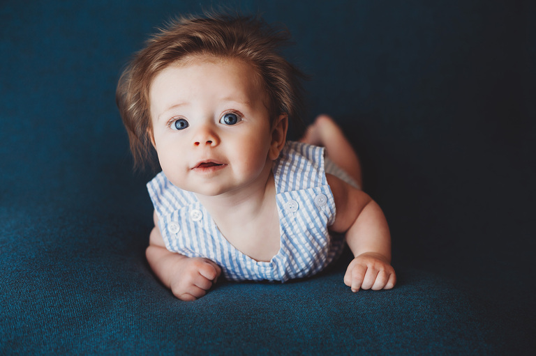 Carter in his cute monogrammed onesie on a blue backdrop to match his eyes during his three-month session