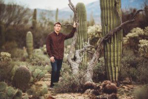 Cory leaning against an old dead tree near two lovely saguaros