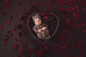Baby O in a Valentine's Day themed setup featuring a heart bowl and red rose petals by Wiesbaden newborn photographer