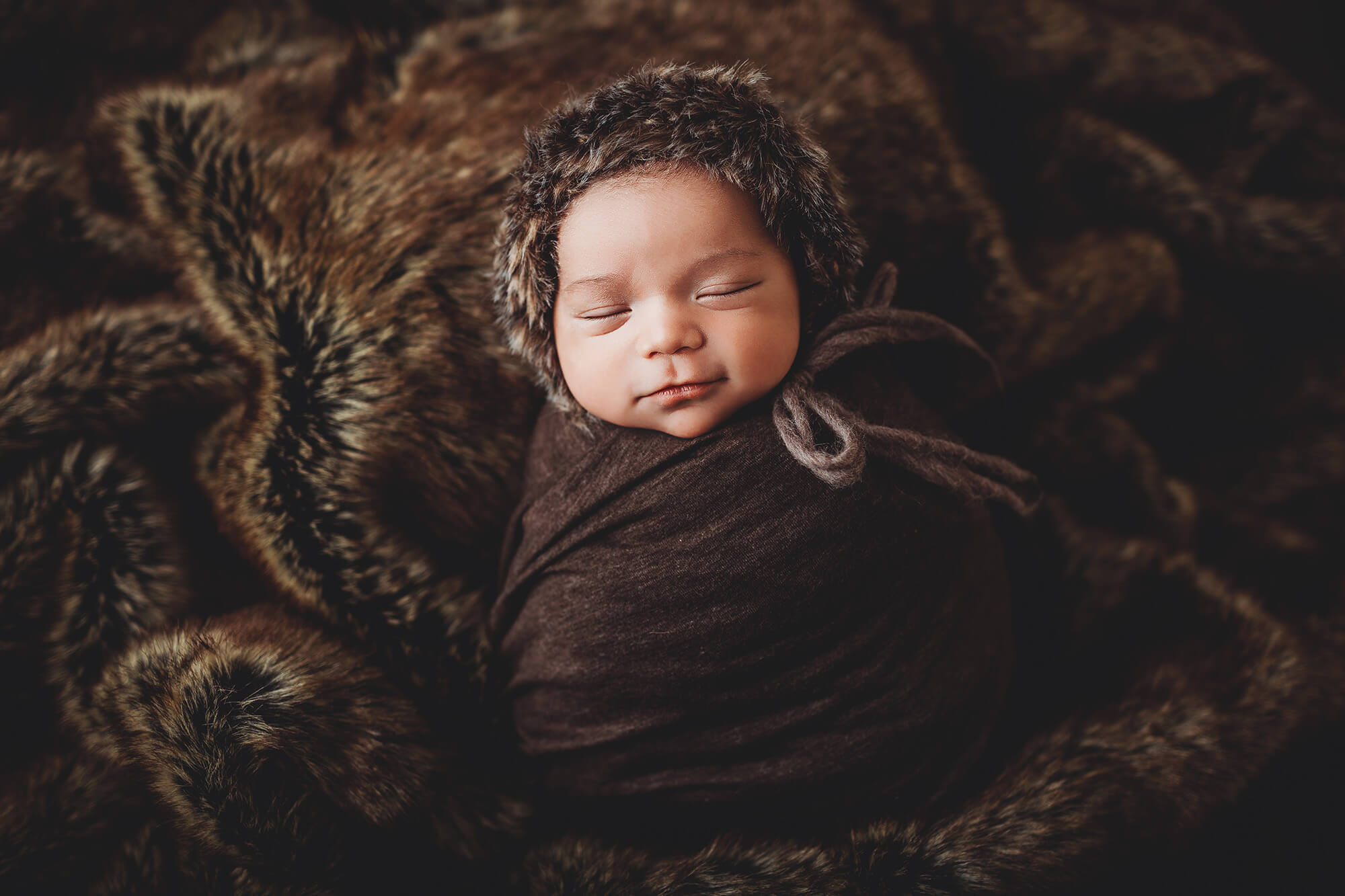 Newborn baby boy wrapped in brown and fur, smiling