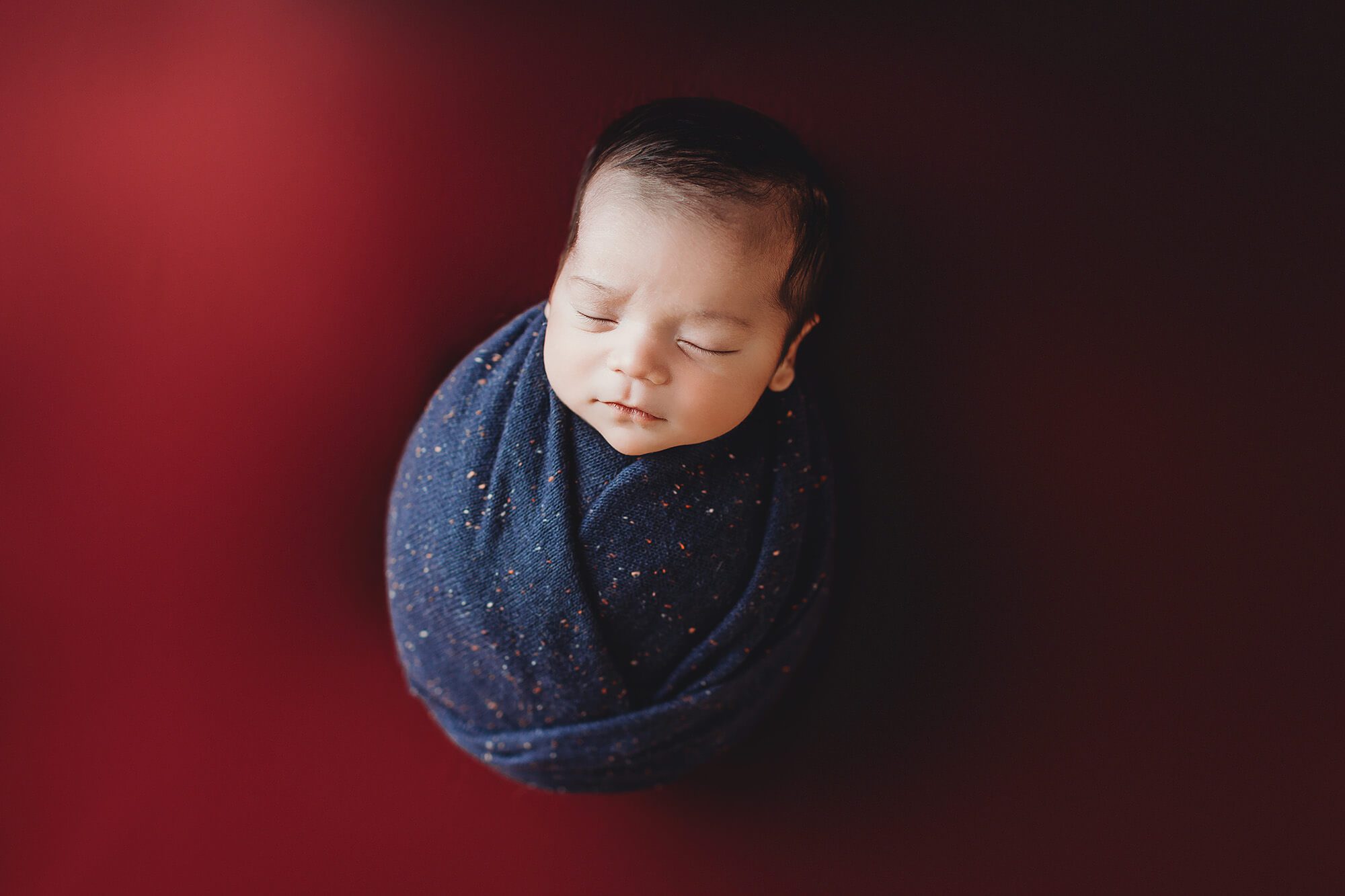 Oliver wrapped in blue on a red blanket