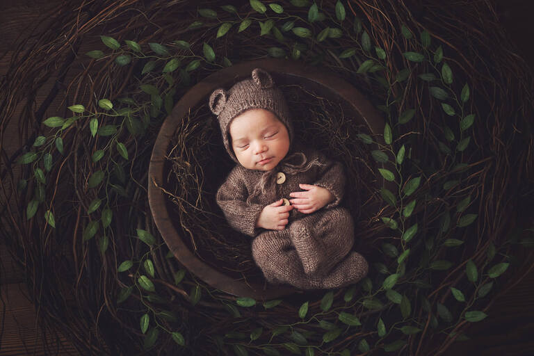 Newborn baby boy Oliver amongst greenery in a bear onesie.